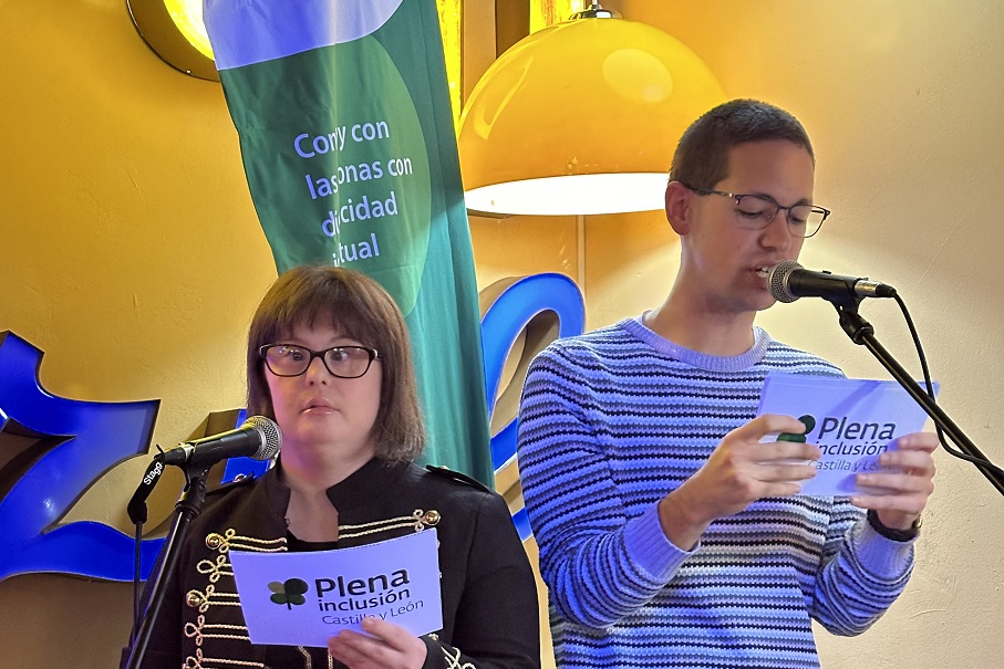 Dos personas con discapacidad intelectual hablan frente a un micrófono. En su mano sostienen tarjetas con el logo de Plena inclusión Castilla y León