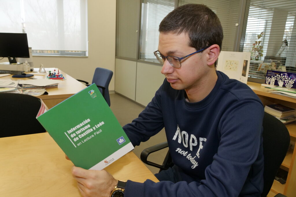 Chico joven está sentado leyendo el folleto turístico en lectura fácil de Castilla y León
