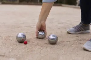 Una mano coge una de las tres bolas de petanca que hay en el suelo