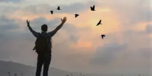 Persona con los brazos en alto mirando el cielo y unos pájaros volando